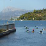 Kayaking Poros, Greece. A small group of kayaks paddle towards a mountain in the distance.
