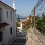 A narrow alley between white houses with a view of the sea.
