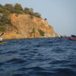 A rocky cliff by the sea with boats on the water.