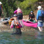 People preparing kayaks by the shore with one person in the water.