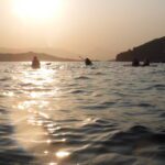 People kayaking on a calm sea at sunset.