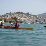 White Greek buildings in the distance, while a kayaker paddles in the foreground.