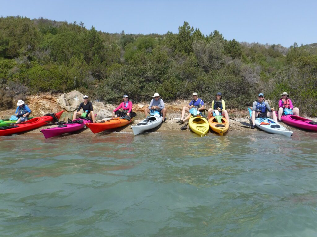 DSCF0571-1024x768 (1) A group of people kayaking in calm water near a forested shore.
