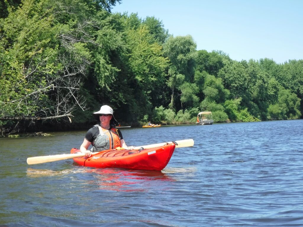 A person kayaking on a river surrounded by green trees.