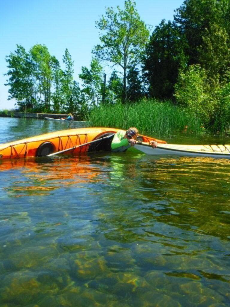 DSCF1884-768x1024 Two kayaks resting on clear water near a lakeshore with green trees.