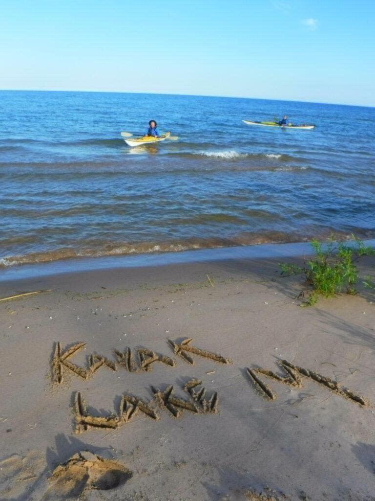 DSCF2307-768x1024 Words written in sand at a beach with two people kayaking in the water.