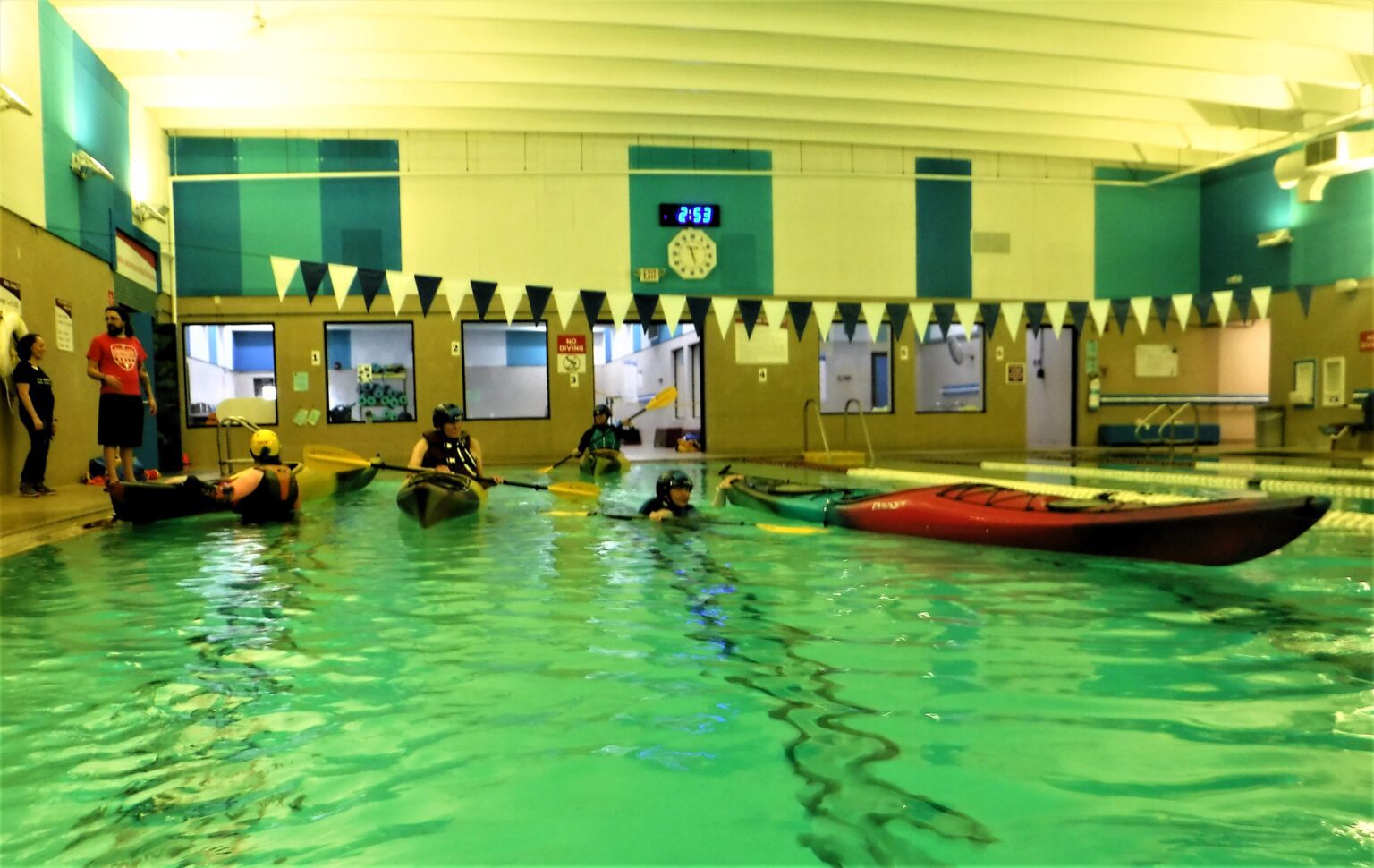 DSCF3967-1536x970 (1) People enjoying a swim in an indoor pool with kayaks nearby.