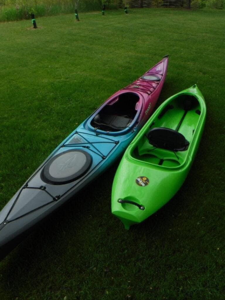 DSCF4200-768x1024 (1) Two kayaks, one red and one green, on grass.