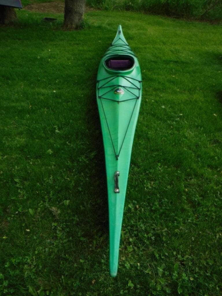 DSCF4202-768x1024 A green kayak on grass with black bungee cords and a seat.