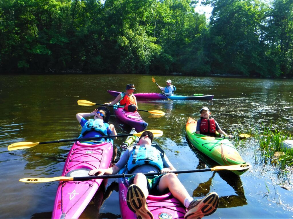 DSCF4259-1024x768 A group of people kayaking on a calm river surrounded by trees.