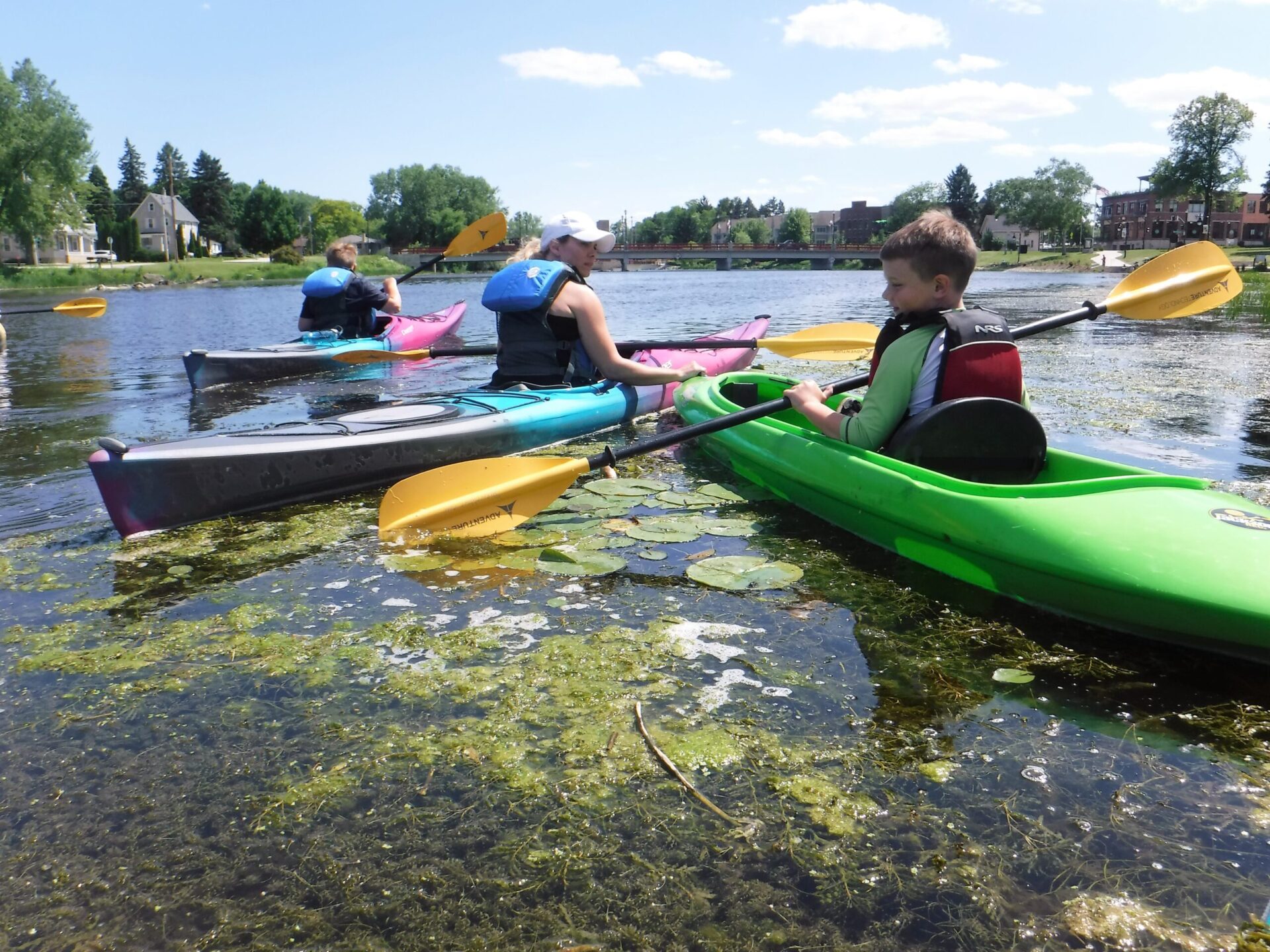 Three people kayaking on a river under a clear sky.