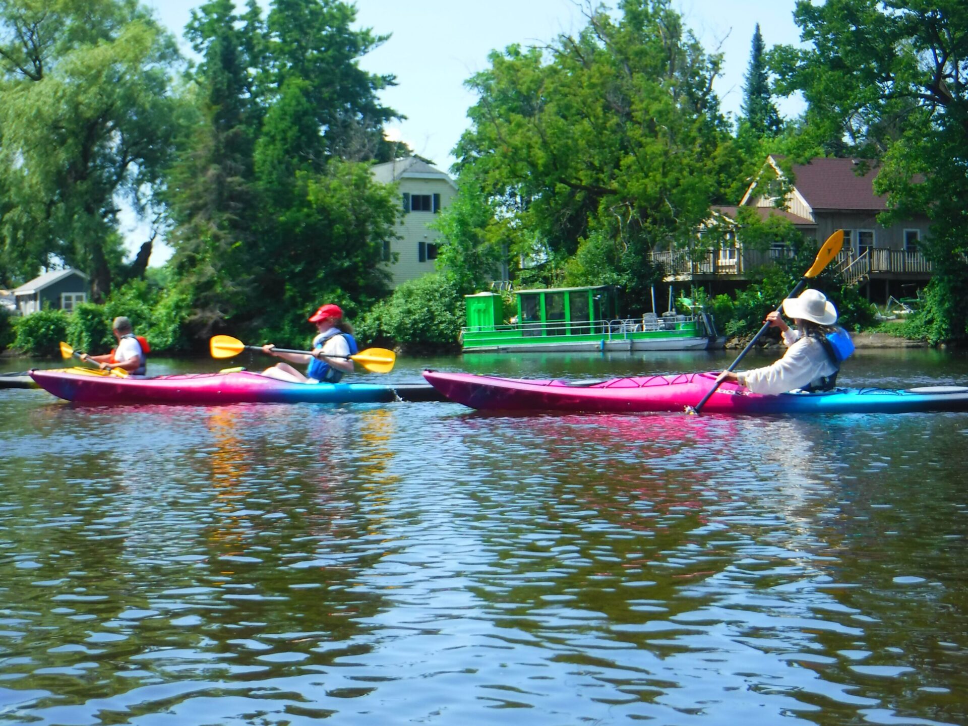 DSCF4505-scaled Two people kayaking on a calm river surrounded by greenery.