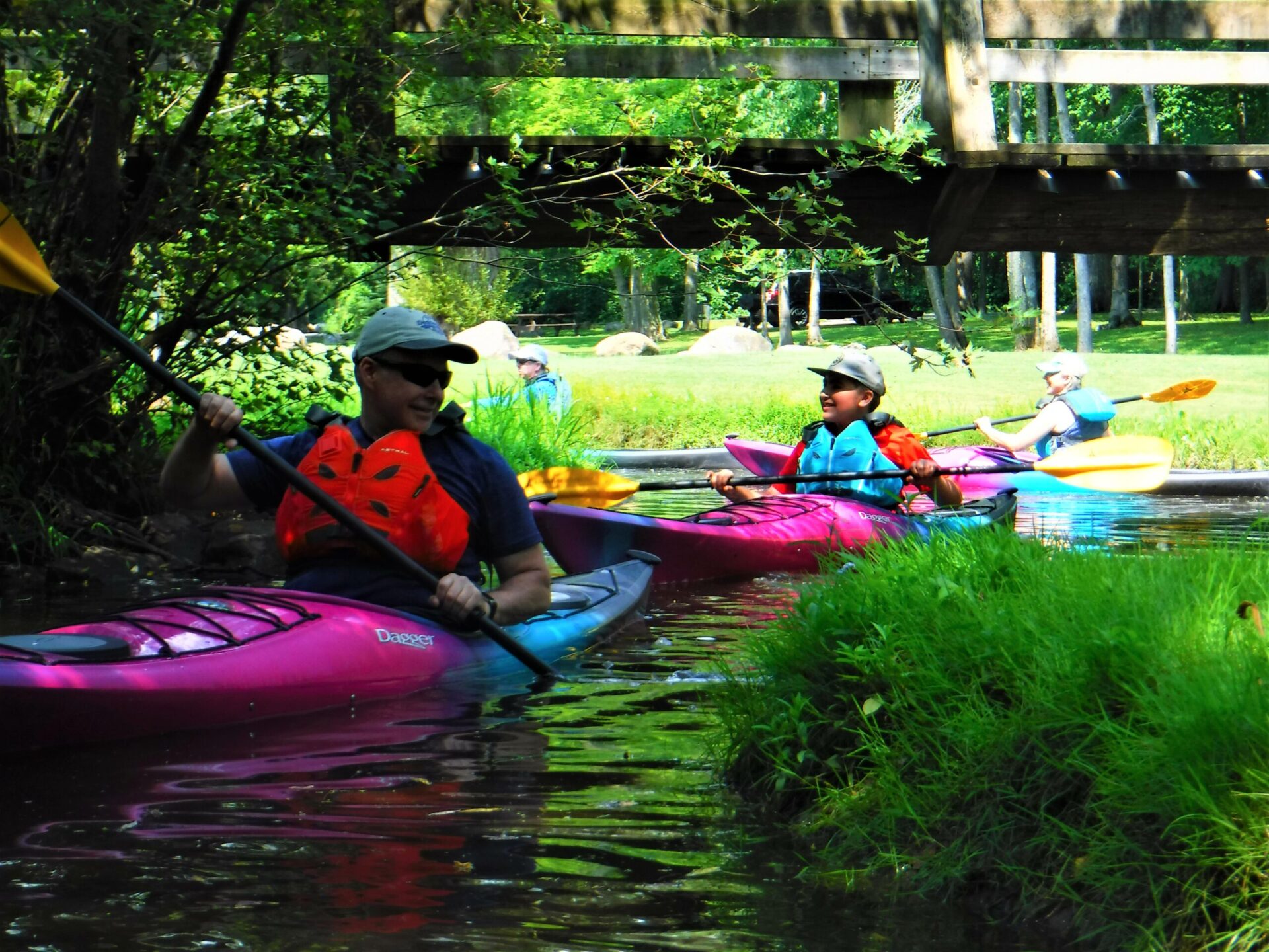 Two people kayaking on a calm river surrounded by greenery.