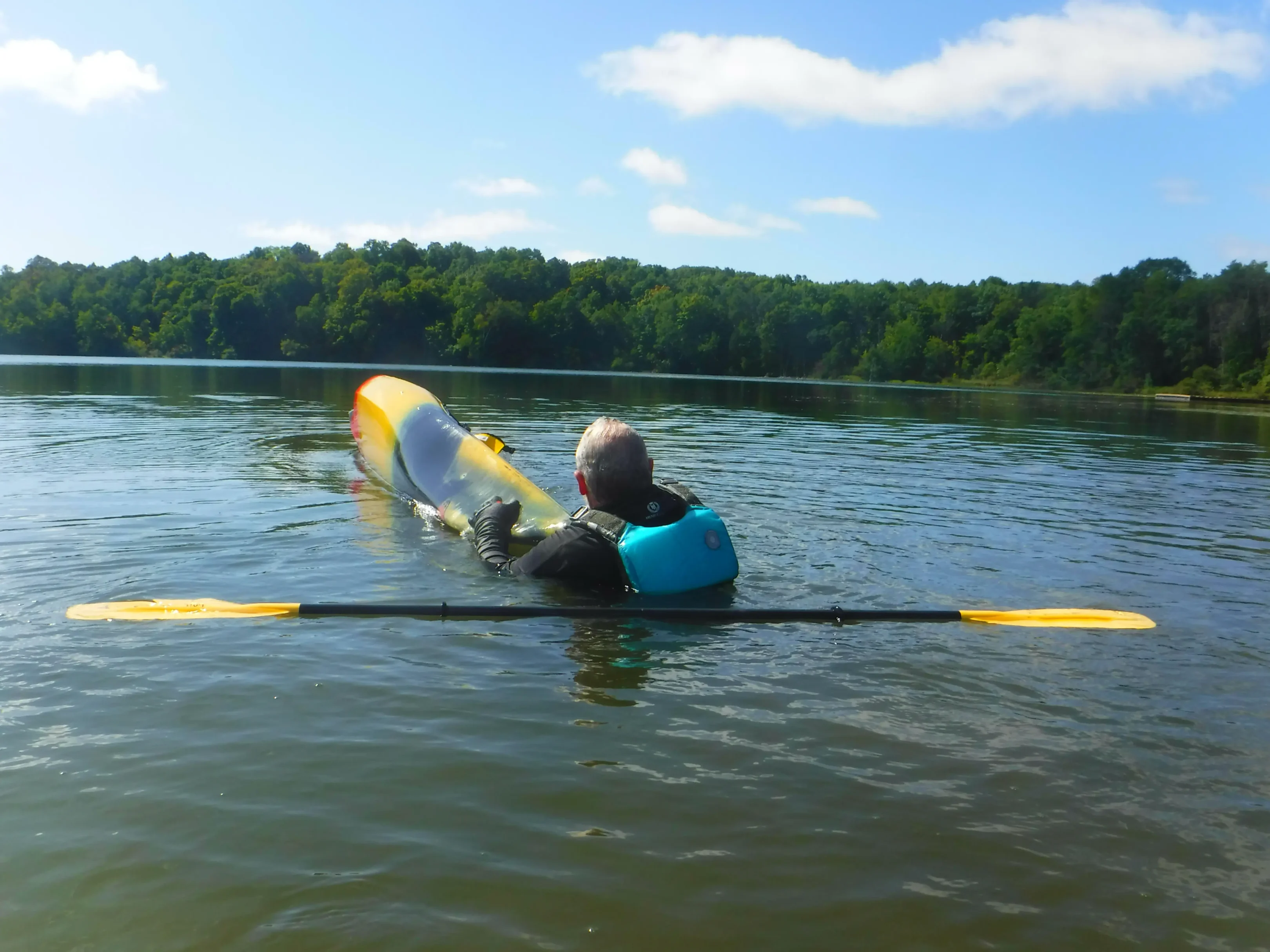 DSCF4636-scaled A person in a kayak holding a dog over the water.