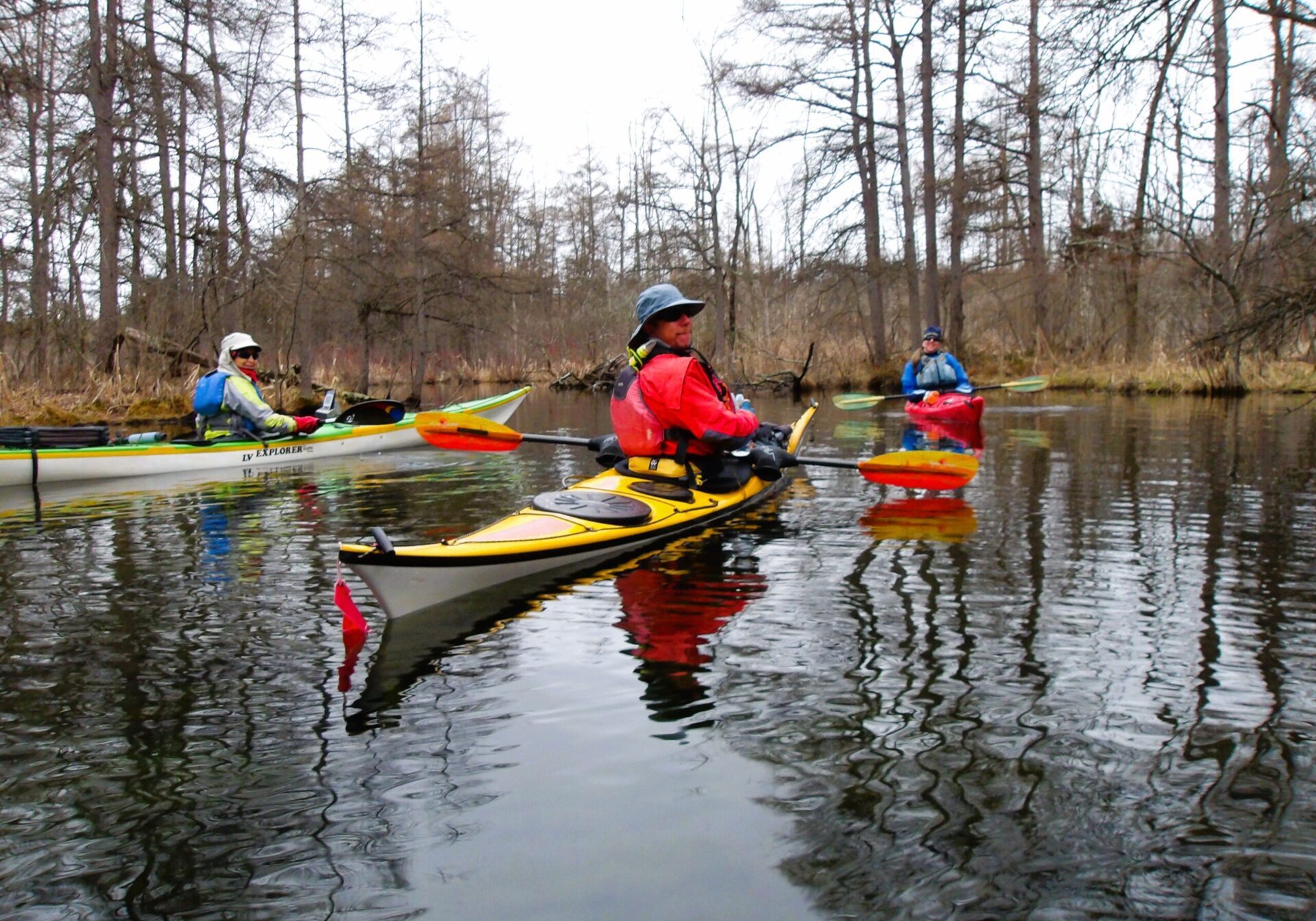 kayaks by the blue hole Three people kayaking on a calm river surrounded by bare trees.