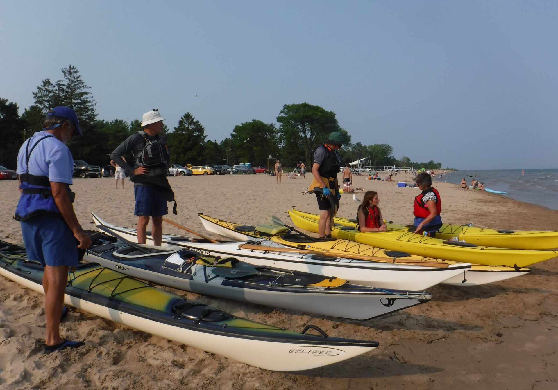 a group is near their sea kayaks on the sand, before the paddle on Lake Michigan