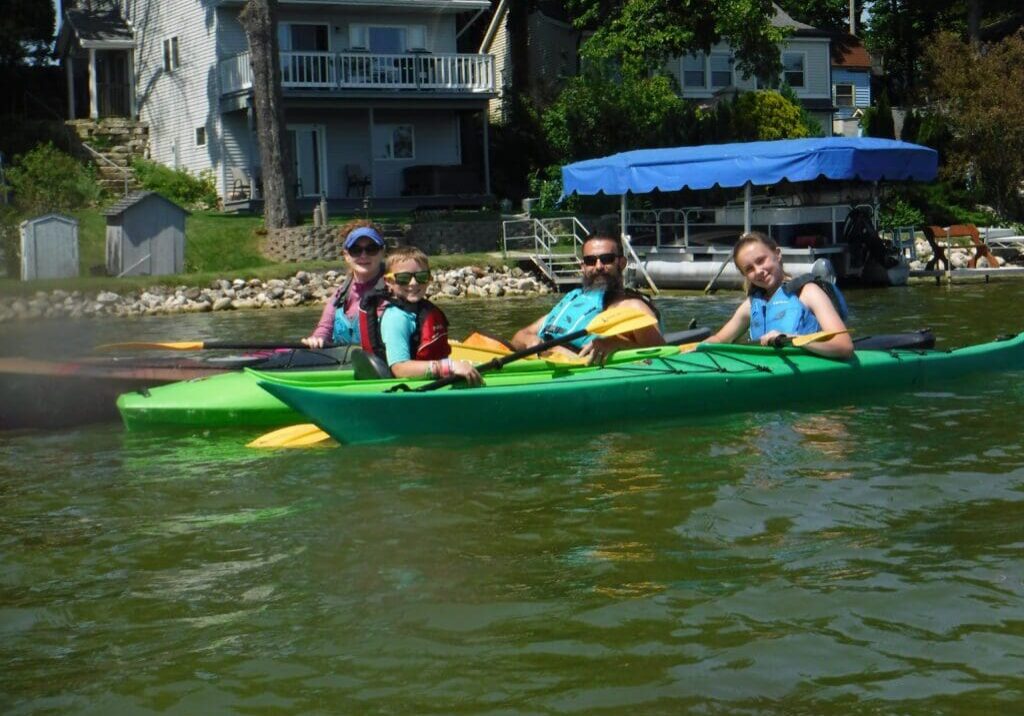 Four people kayaking on a lake near houses.
