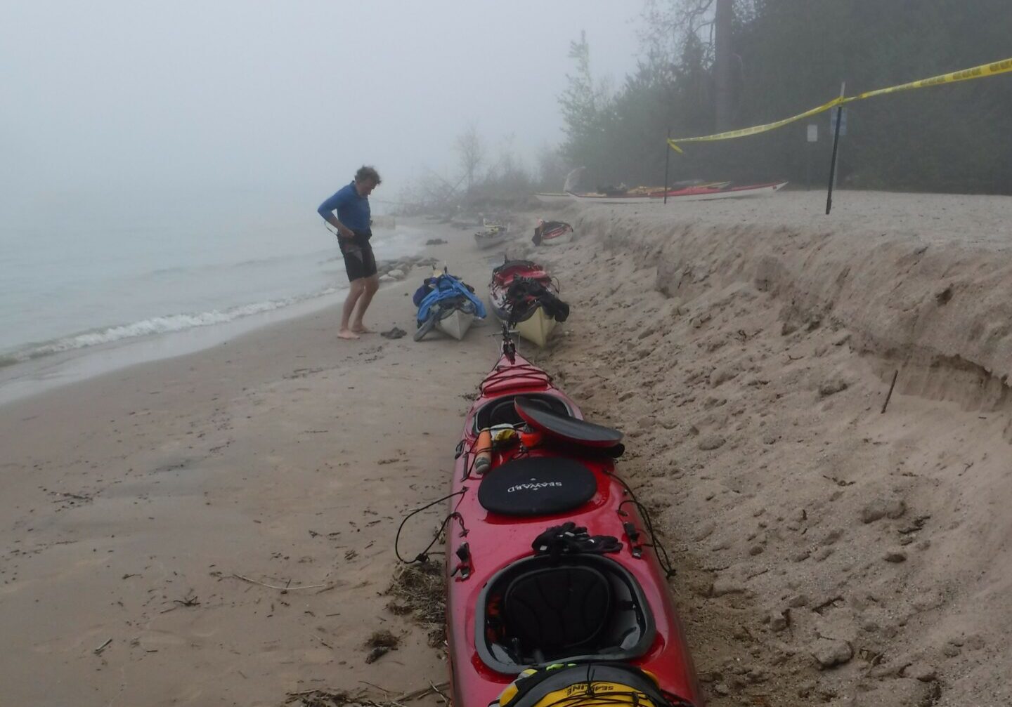 a man standing on the beach next to his kayak, the sky is very foggy